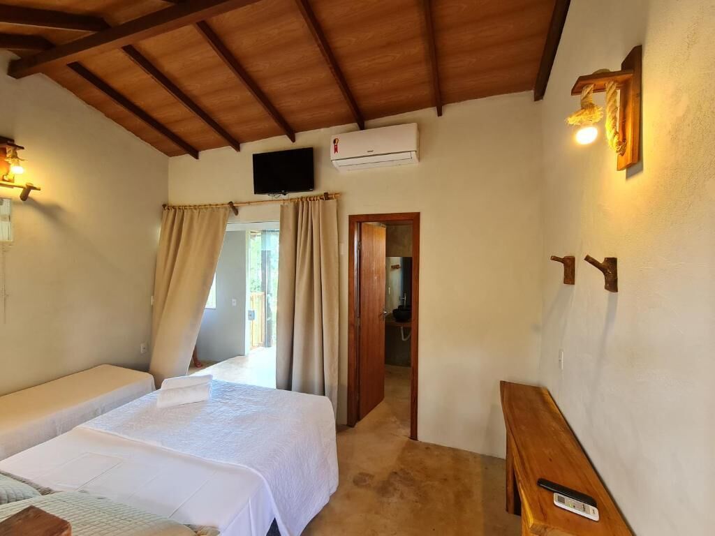 A bedroom with two beds, a wooden ceiling, an air conditioning unit, a television, and a wooden bench.