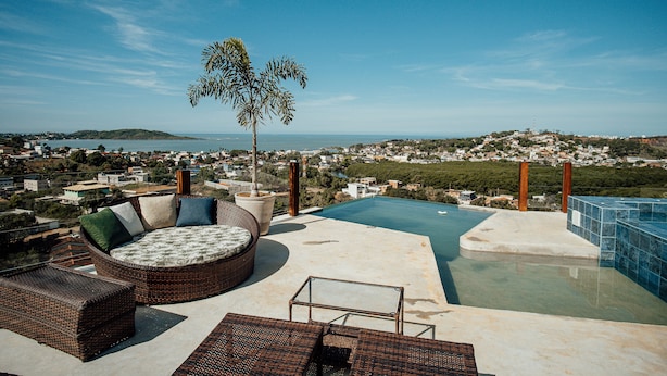 Una piscina infinita en la azotea con muebles de mimbre y vistas a la ciudad.