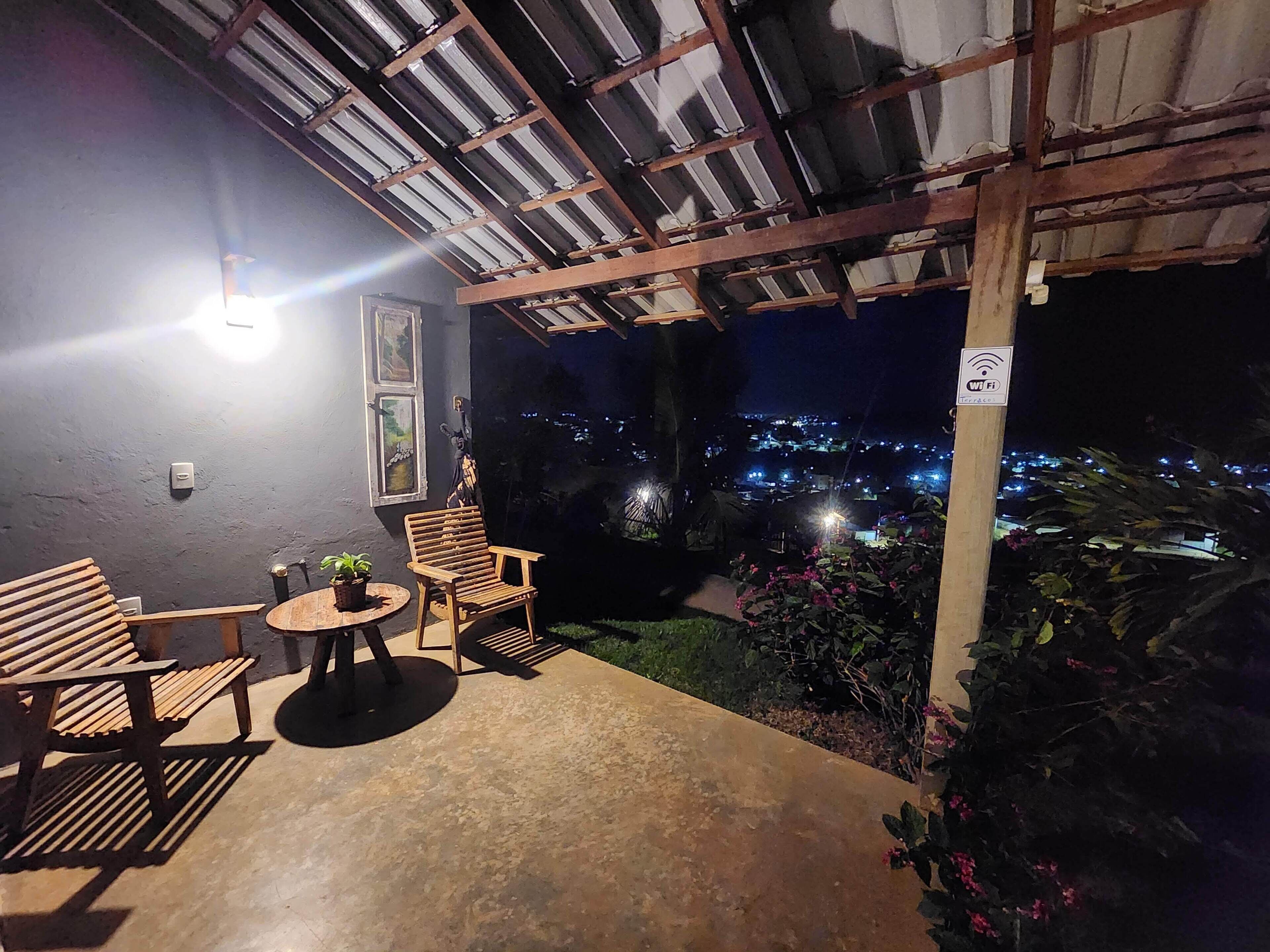 Un espacio de estar al aire libre cubierto con una mesa, sillas, una planta en maceta y vistas a un paisaje urbano nocturno.
