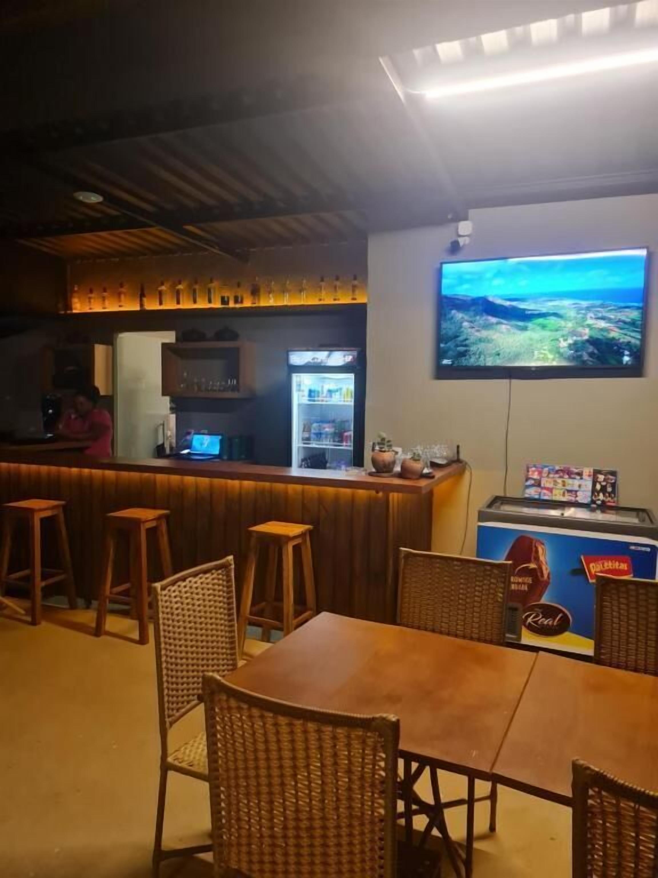 Zona de bar con taburetes, un refrigerador y un televisor mostrando un paisaje.