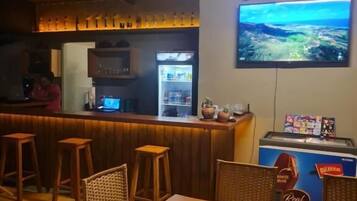 Zona de bar con taburetes, un refrigerador y un televisor mostrando un paisaje.