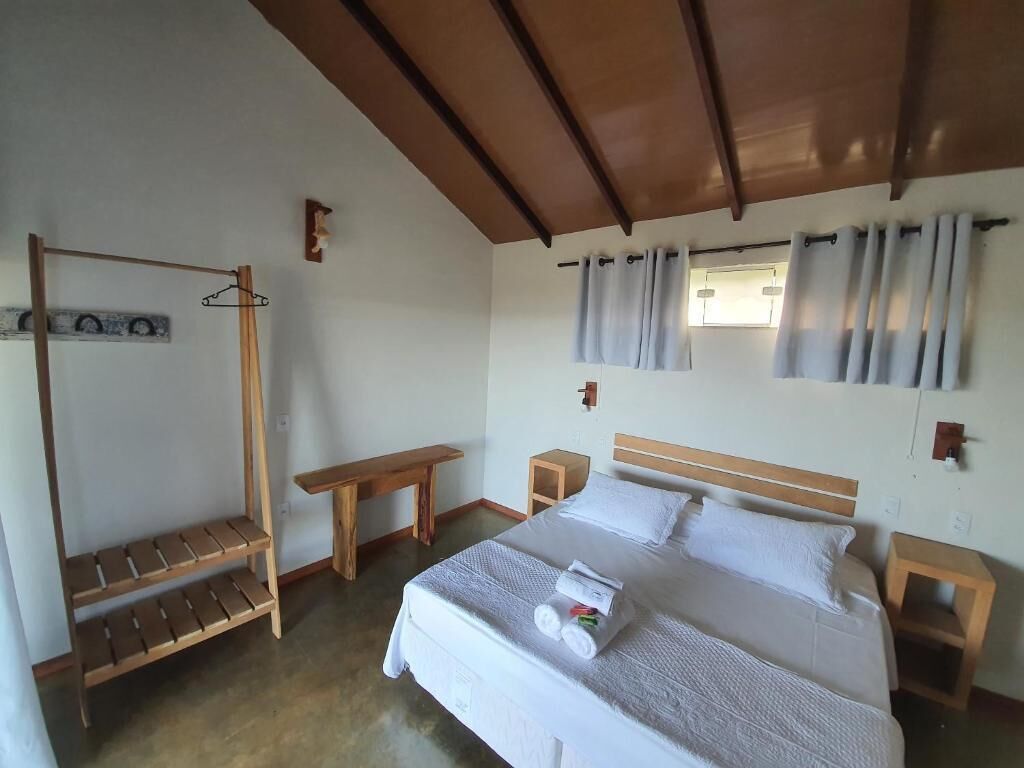 Un dormitorio con cama, un banco de madera, una mesita y un perchero.