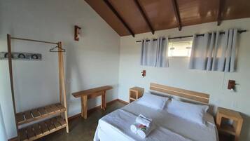 A bedroom with a bed, a wooden bench, a small table, and a hanging clothes rack.
