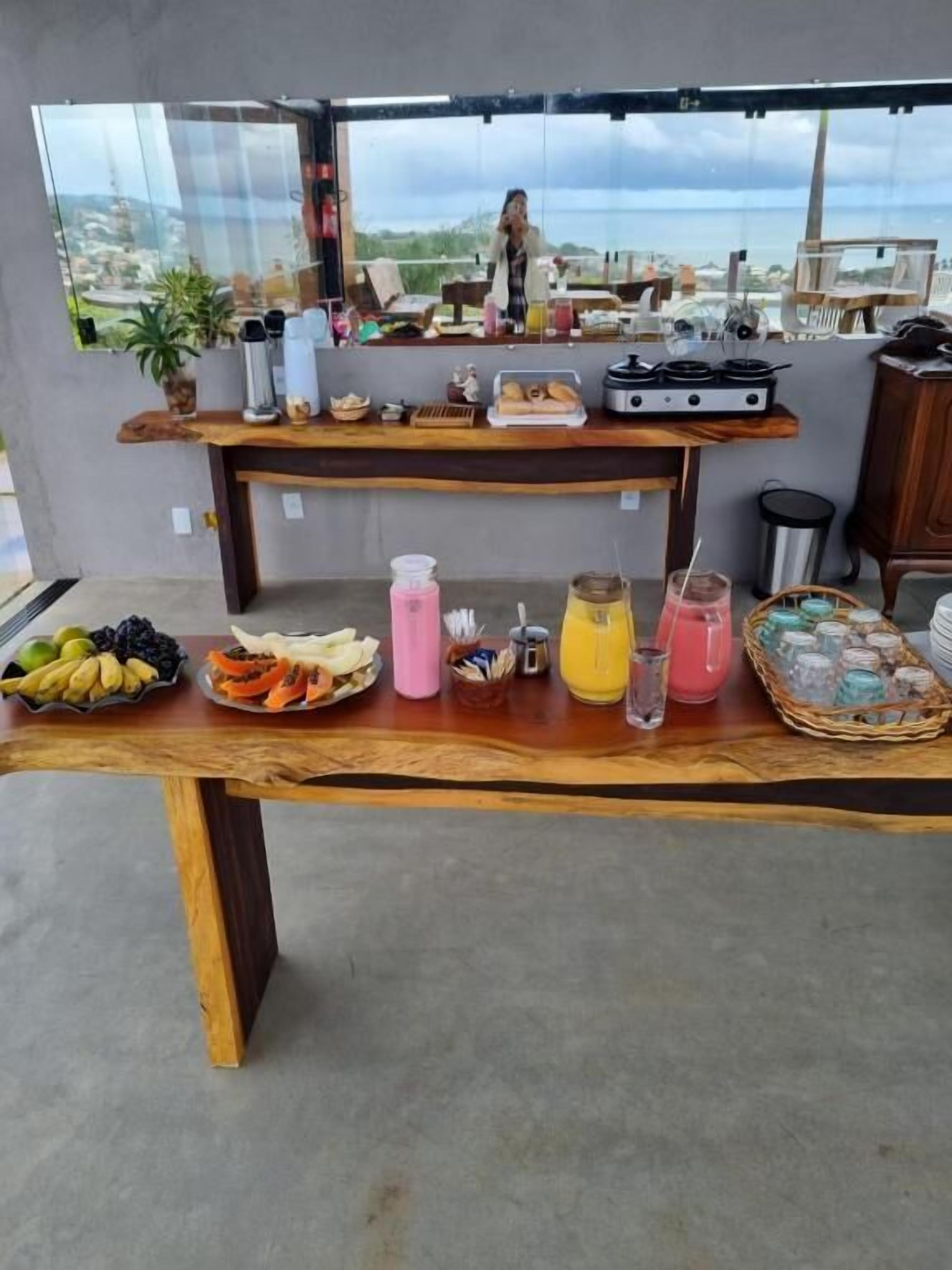 A buffet table with various food items and beverages, a coffee maker, and a view of the ocean through a large window.