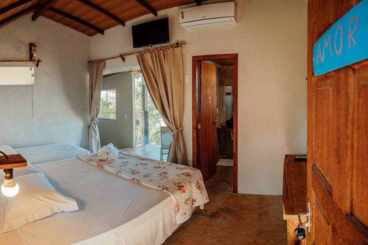 A bedroom with a bed, a television, an air conditioning unit, and a door with a sign.