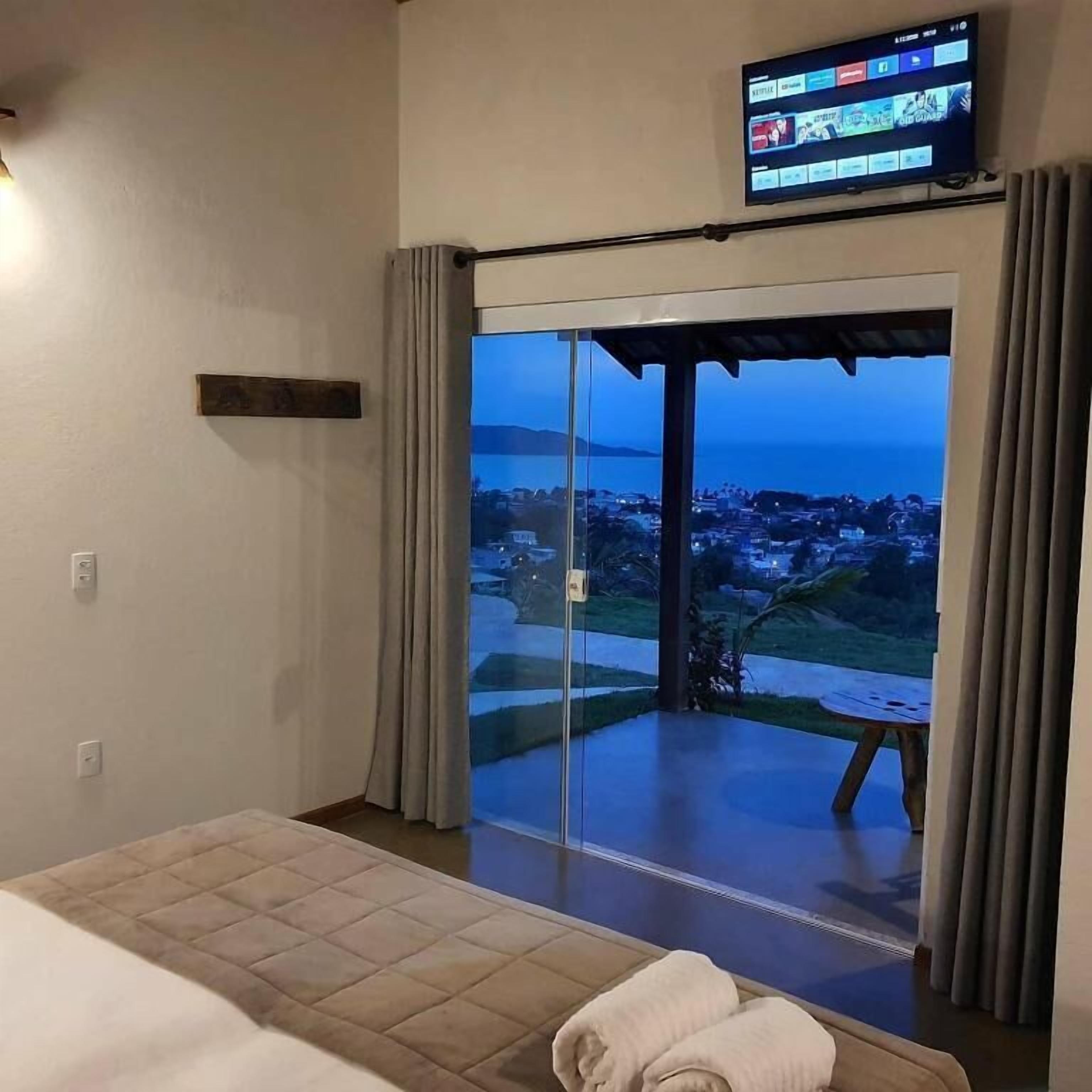 Habitación de hotel con cama, televisor montado en la pared y puerta corrediza de vidrio que da a un balcón con vistas a la ciudad.