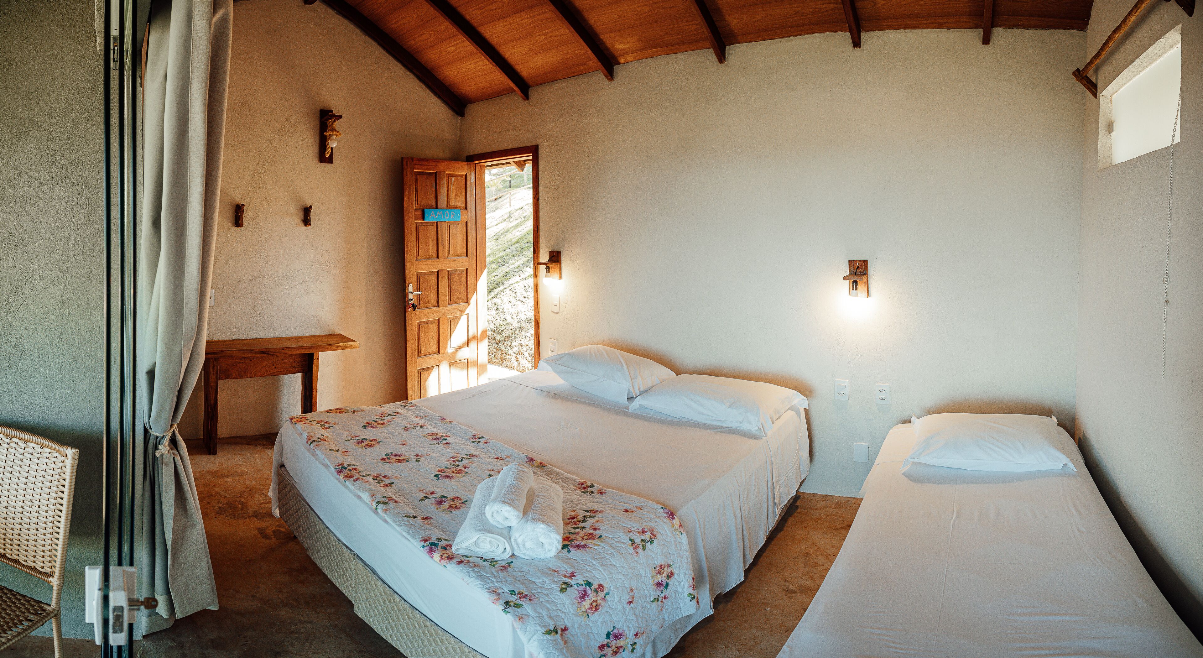 Un dormitorio con dos camas, una puerta de madera, una mesita pequeña y una silla de mimbre.