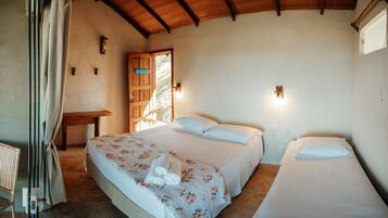 Un dormitorio con dos camas, una puerta de madera, una mesita pequeña y una silla de mimbre.