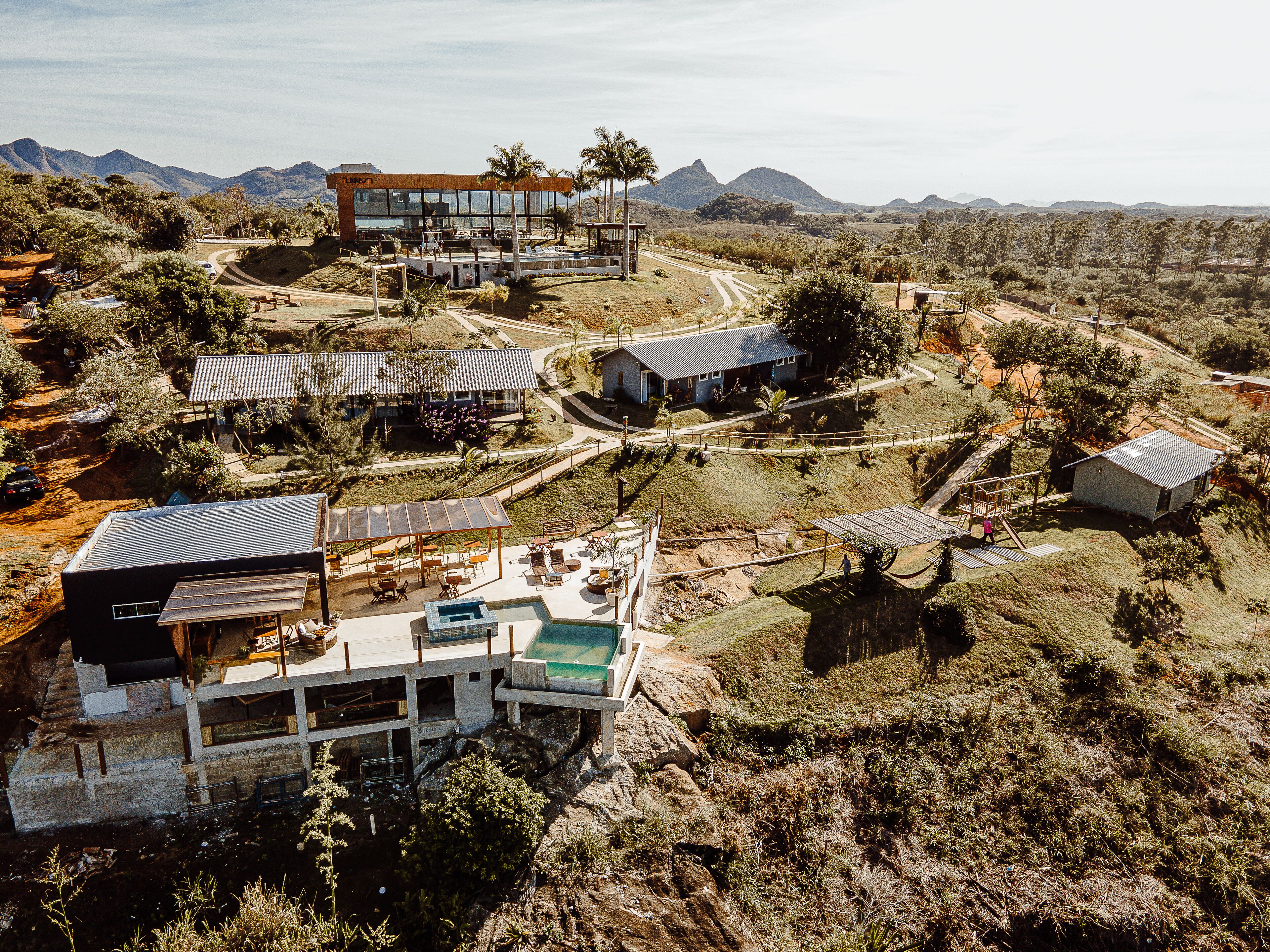A modern resort with multiple buildings, a swimming pool, and a mountainous backdrop.