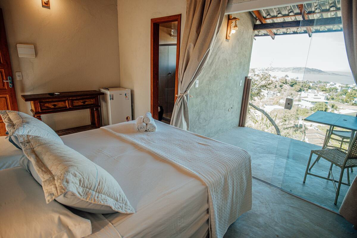 A bedroom with a bed, a desk, and a view of a balcony with a table and chair.