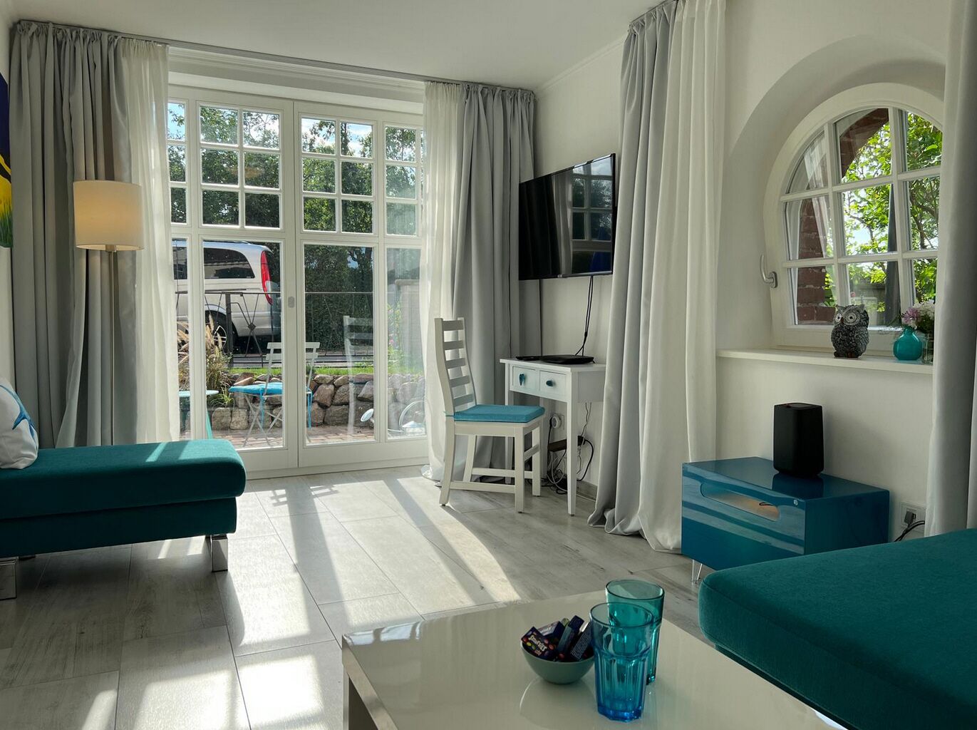 Una habitación con sofá, escritorio con computadora, televisor y ventana con cortinas.