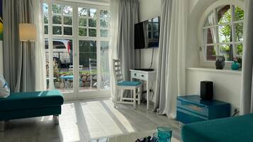 Una habitación con sofá, escritorio con computadora, televisor y ventana con cortinas.