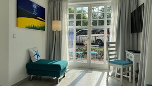 Habitació amb un llit color turquesa, una cadira, un televisor i un finestral gran que ofereix vistes a cotxes aparcats i vegetació a l'exterior.