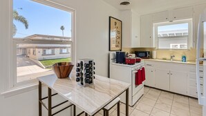 Una cocina con vistas a un barrio residencial, un cuenco de madera, una botellera, una estufa, un microondas y un lavabo.