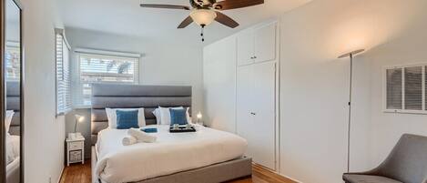 Un dormitorio con cama, ventilador de techo, una silla y armario.