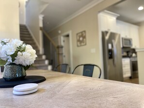 Comedor con mesa de madera, flores blancas en un florero y un posavasos negro.