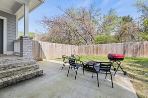 Un patio con una parrilla, mobiliario exterior y una valla de madera.