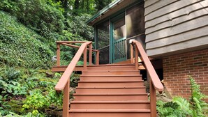 Eine hölzerne Treppe führt zu einem Gebäude mit einer grünen Tür, umgeben von üppiger Vegetation.