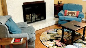 Ein Wohnzimmer mit Kamin, Fernseher, einem blauen Sofa und einem gemusterten Teppich.