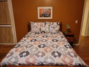 Een slaapkamer met een bedovertrek met patroon, een houten hoofdbord, een ingelijst schilderij aan de muur en een nachtkastje met een lamp.