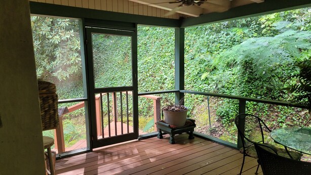 Eine überdachte Veranda mit Holzboden, einem Tisch, einem Stuhl und einem Blumentopf.