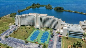 Ett högt hotell med en tennisbana och en parkeringsplats, omgivet av vatten och grönområden.