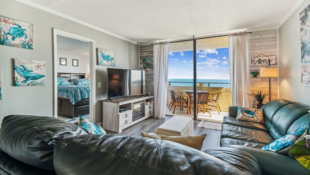 Ett modernt vardagsrum med en soffa i läder, en platt-TV och en matplats med utsikt över havet.