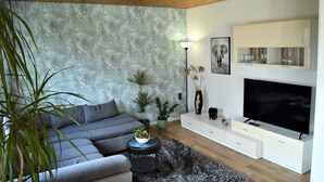 Un soggiorno moderno con un divano grigio, una TV a schermo piatto, un mobile bianco e una parete decorata.