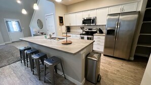 A modern kitchen with a large island, stainless steel appliances, and bar stools. - It's all about Location! This Downtown Retreat = easy access to the heart of GJ. (Grand Junction)