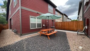 A red house with a wooden deck, a picnic table, and a green umbrella. - It's all about Location! This Downtown Retreat = easy access to the heart of GJ. (Grand Junction)