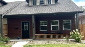 A two-story house with a dark red exterior, a front porch with a wooden railing, and a small garden area with a pathway leading to the front door. - It's all about Location! This Downtown Retreat = easy access to the heart of GJ. (Grand Junction)