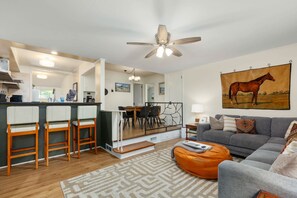 A modern living room with a grey sofa, orange bean bag, and a dining area with a bar.
