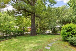 A well-maintained garden with a large tree, a stone pathway, and a neatly trimmed hedge.