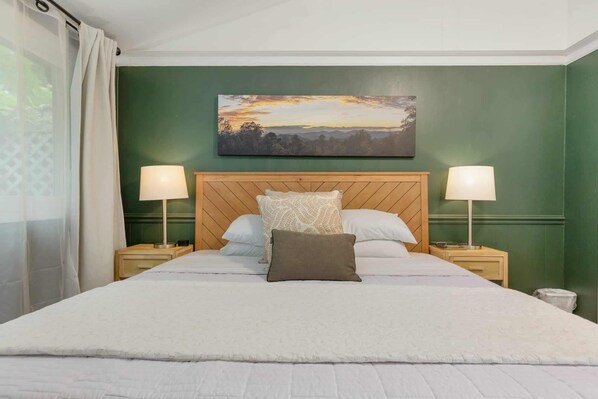 A neatly made bed with a wooden headboard, two bedside lamps, and a painting above it.