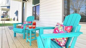 Une véranda avec deux fauteuils Adirondack turquoise, chacun agrémenté d’un coussin à motifs floraux, et une petite table avec des boissons.