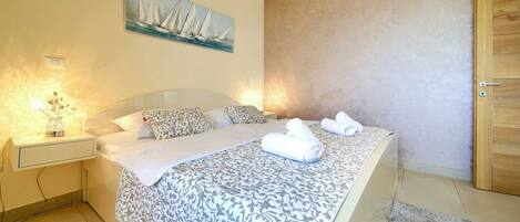 A bedroom with a bed, bedside tables, a painting, and a door.