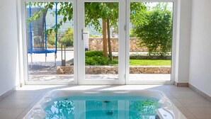 A hot tub in a room with a view of a garden and a blue swing set. - Apartment ROYAL 1 with pool and jacuzzi (Kornić)