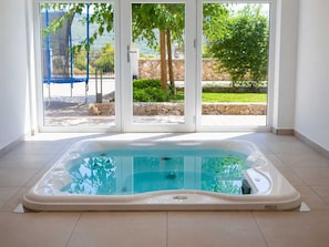 A hot tub in a room with a view of a garden and a blue swing set. - Apartment ROYAL 1 with pool and jacuzzi (Kornić)
