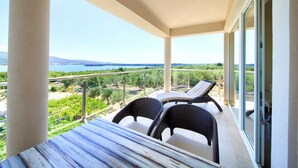 A balcony with a view of the sea and greenery, two wicker chairs, and a wooden table. - Apartment ROYAL 1 with pool and jacuzzi (Kornić)