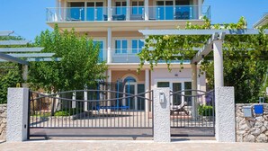 A two-story building with a gated entrance, a balcony on the upper floor, and a stone wall with a blue mailbox. - Apartment ROYAL 1 with pool and jacuzzi (Kornić)