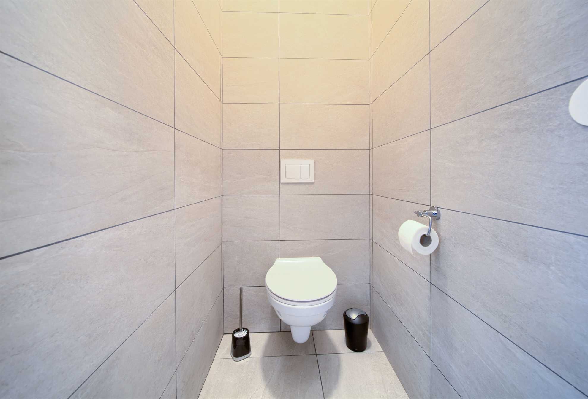 A small, modern bathroom with a toilet, a trash bin, a toilet paper holder, and a light switch on the wall.
