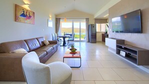 Una sala de estar moderna con un sofá, una mesa baja con fruta, un televisor de pantalla plana y un balcón con vistas.