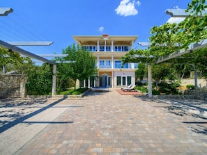 A two-story building with a covered entrance, a stone wall, and a paved driveway leading to a seating area with sun loungers. - Apartment ROYAL 2 with pool and jacuzzi (Kornić)