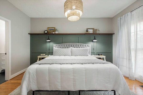 A bedroom with a large bed, two bedside tables, a green headboard, and a hanging light fixture.