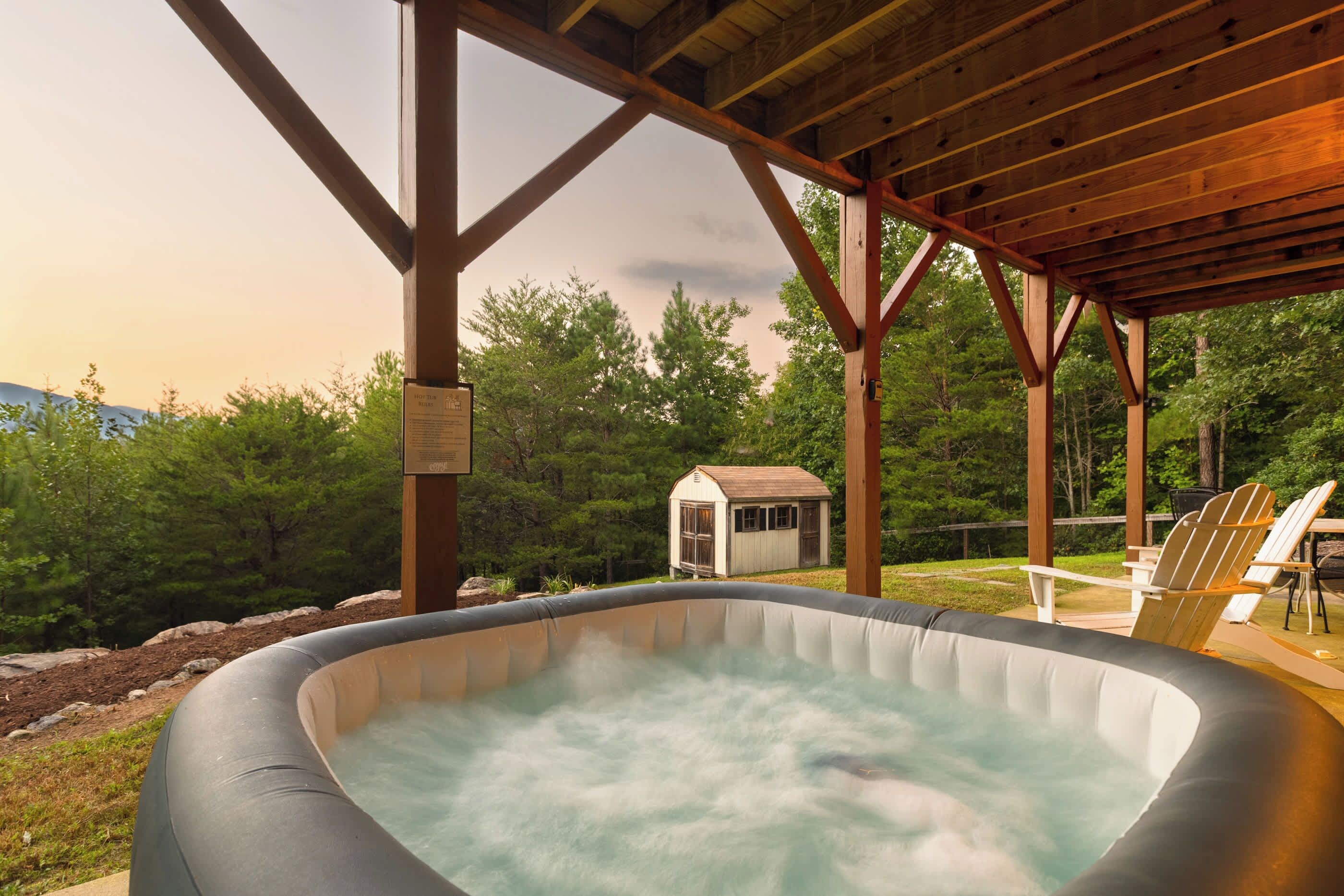 A hot tub under a wooden pergola with a view of a small shed and trees.