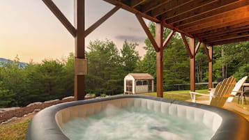 A hot tub under a wooden pergola with a view of a small shed and trees.