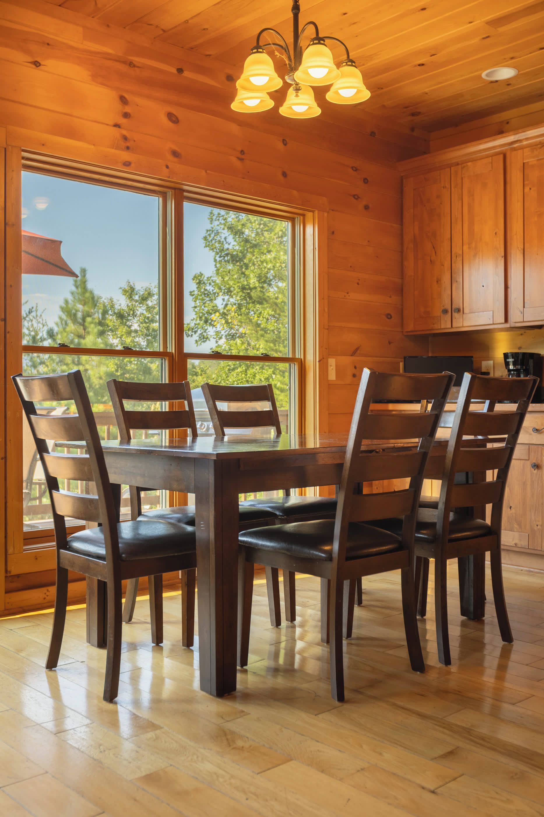 A wooden interior with a dining table and chairs, large windows, and a kitchen area.