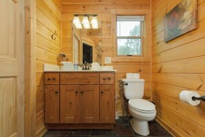 A wooden cabin bathroom with a wooden vanity, a toilet, and a window. - Sunset mountain views, hot tub and fenced yard (Mill Spring)
