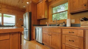 A wooden cabin kitchen with a refrigerator, dishwasher, and wooden cabinets. - Mountain View Cabin|Hot Tub|Fenced Yard for Pets (Mill Spring)