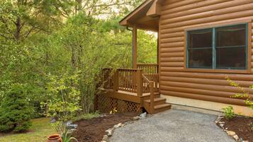 A wooden cabin with a porch, a window, and a stone pathway leading to the entrance.